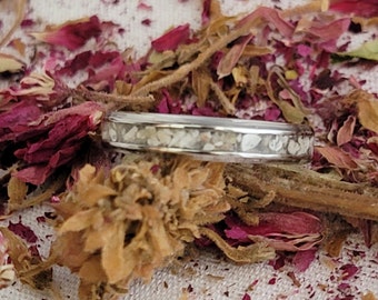 May include: A silver ring with a thin band and a line of white sand embedded in the metal.