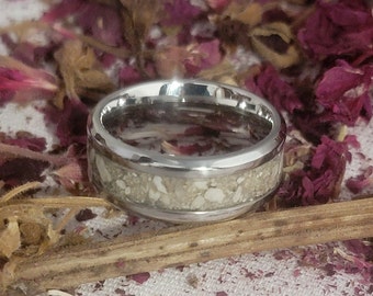 May include: A silver ring with a white inlay of crushed seashells. The ring is on a background of dried rose petals.