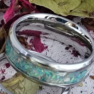 May include: A silver ring with a green and blue opal inlay. The ring is on a fabric background.