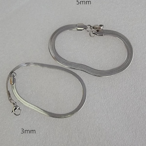 May include: Two silver-colored herringbone chain bracelets. One bracelet is 5mm wide, and the other is 3mm wide. Both bracelets have a lobster clasp closure. The bracelets are displayed on a light gray surface.