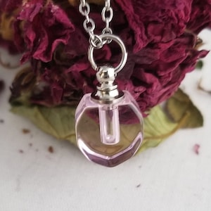 May include: A silver chain necklace with a pink glass perfume bottle pendant. The bottle has a silver cap and a clear glass tube inside.