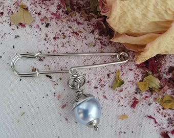 May include: A silver safety pin with a light blue pearl charm attached. The charm is made of metal and has a silver finish.