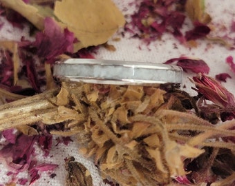 May include: A silver ring with a white inlay. The ring is surrounded by dried flower petals.