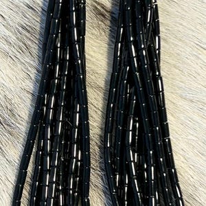May include: A pair of long dangle earrings featuring multiple strands of glossy black cylindrical beads suspended from polished silver-tone metal caps. Each earring is attached to a simple silver-tone hook wire for pierced ears.