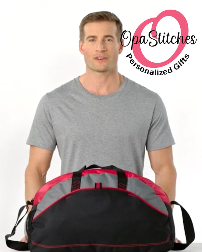 May include: A black and gray duffel bag with red accents. The bag has a zippered main compartment and a front pocket. The bag is being held by a person.