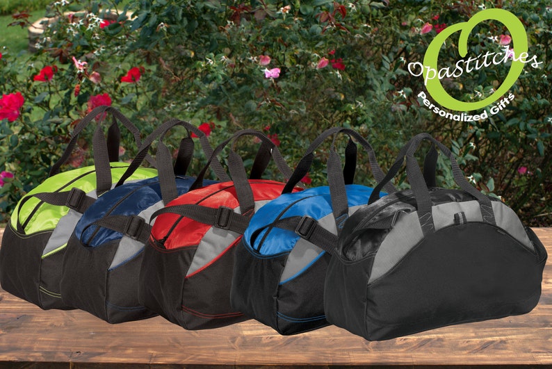 May include: Five different colored duffel bags with black handles and straps. The bags are lined up on a wooden surface. The bags are all the same size and shape. The bags are made of a durable, water-resistant material.  Opastitches Personalized Gifts.