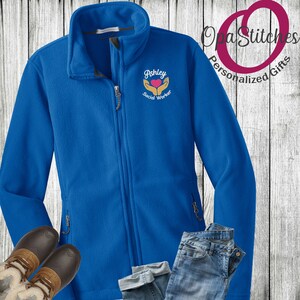 May include: Royal blue fleece jacket with a zipper closure. The jacket has an embroidered design on the left chest that says "Ashley Social Worker" with a heart and hands.