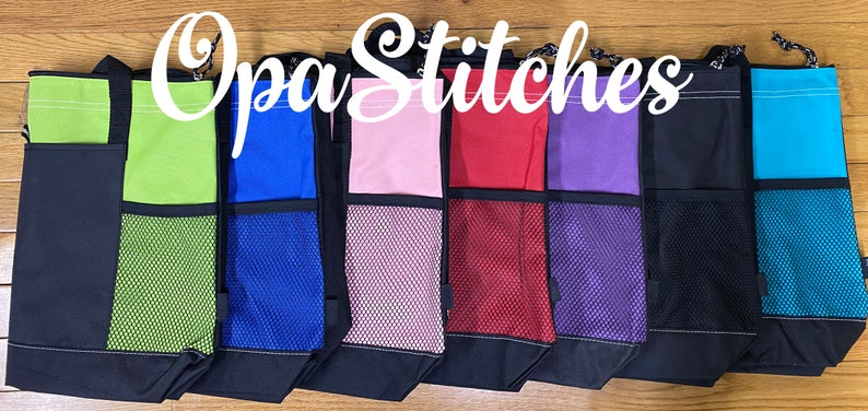 May include: A row of eight tote bags with different colored fabric panels and mesh pockets. The bags are all black with a drawstring closure. The text " Opa Stitches" is written in white cursive across the top of the image.