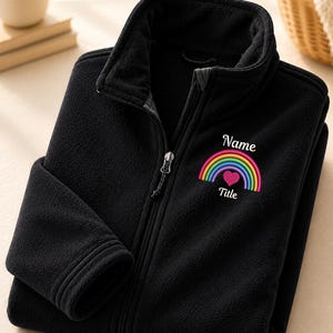 May include: A black fleece jacket with a full-length front zipper and a high collar. The chest features an embroidered design of a colorful rainbow with a pink heart at its center, accompanied by the white text Name above and Title below.