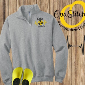 May include: Gray 1/4 zip sweatshirt with a yellow and black radiation symbol and the text "Katie Rad Tech" embroidered on the left chest.