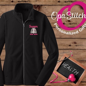 May include: Black fleece jacket with a zipper closure. The jacket has a pink embroidered design of a ribcage with a heart on the left chest. The text "Susan Rad Tech" is embroidered below the design.