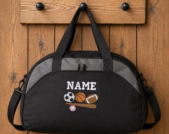 May include: A black and charcoal gray duffel bag featuring the white text NAME above an embroidered graphic of a soccer ball, basketball, football, baseball, and a wooden baseball bat with a small baseball resting on the bat.