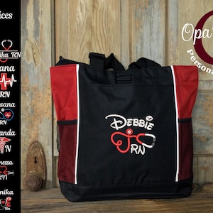 May include: Black and red tote bag with white accents. The bag features the name "Debbie RN" embroidered in white and red, along with a stethoscope design. The bag has side pockets and a handle. The image also shows design choices.
