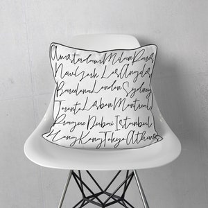 Peut inclure: Un coussin blanc avec des lettres noires en écriture cursive listant différentes villes du monde, notamment Amsterdam, Milan, Paris, New York, Los Angeles, Barcelone, Londres, Sydney, Toronto, Lisbonne, Montréal, Prague, Dubaï, Istanbul, Hong Kong, Tokyo et Athènes.