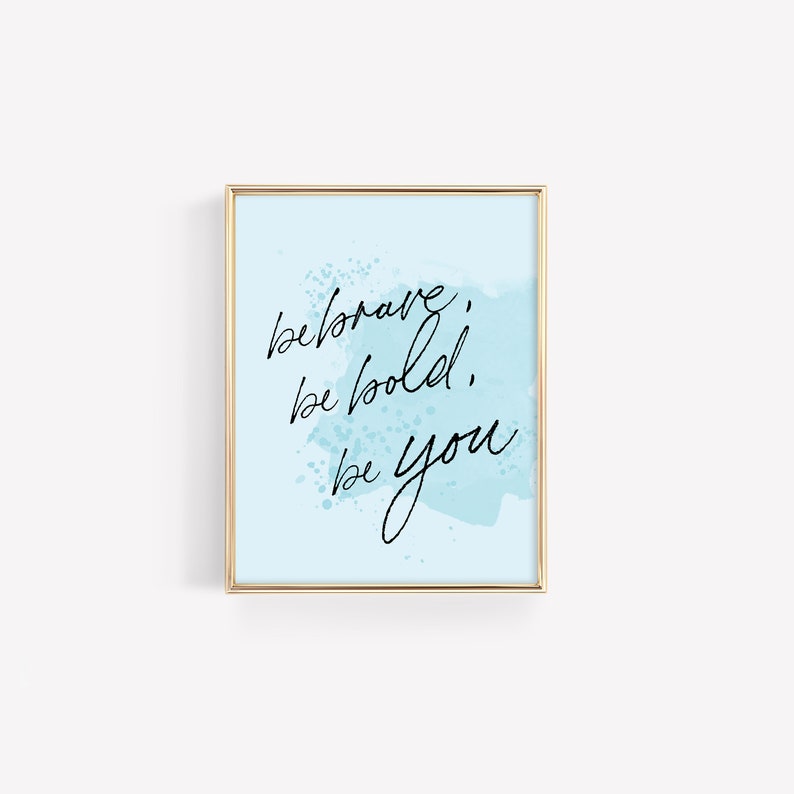 May include: A light blue background with a gold frame and the text "be brave, be bold, be you" in black cursive writing.