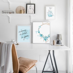 May include: A white desk with a black easel style table and a chair. There are three framed prints on the wall above the desk. The prints are of a woman's face, a bottle of perfume, and a necklace with blue flowers. The text on the print reads "be brave, be bold, be you."