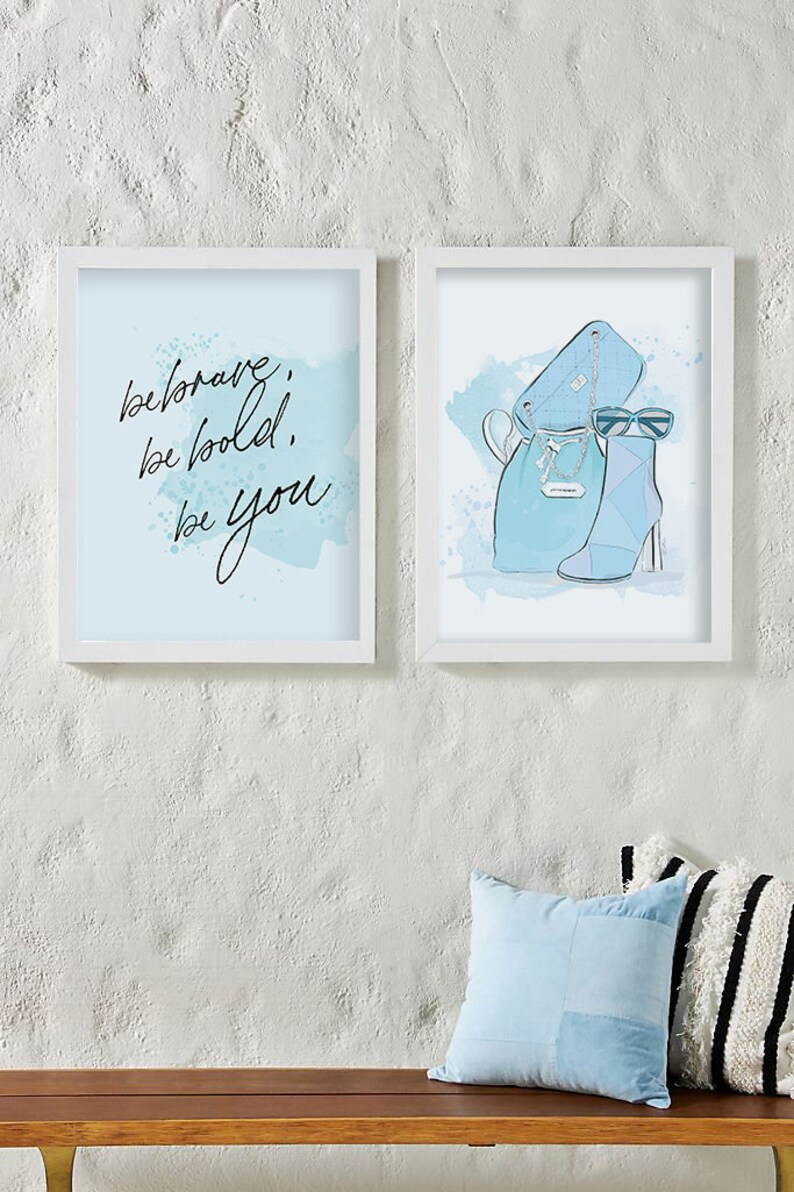 May include: Two framed prints with a blue watercolor background. The left print features the text "be brave, be bold, be you". The right print features a blue handbag, sunglasses, and a blue ankle boot.