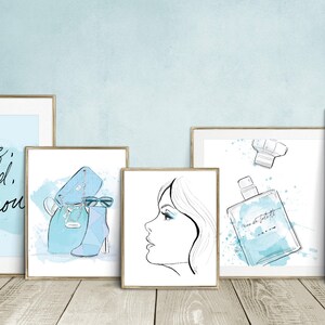 May include: Set of six framed prints with a blue and white watercolor theme. The prints feature a necklace, a quote about being brave and bold, a pair of shoes and a handbag, a woman's face, a bottle of perfume, and a woman in a dress.