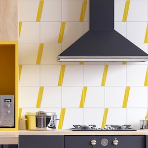 May include: A kitchen with white subway tile backsplash featuring a yellow geometric pattern. A black range hood is mounted above a black gas stove with a stainless steel pot on the counter.