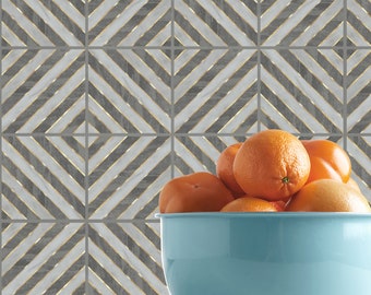 May include: A blue ceramic bowl filled with a variety of orange fruits, including oranges and persimmons. The bowl is sitting on a white surface with a gray and gold geometric patterned background.