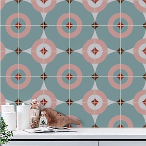 May include: A kitchen backsplash with a repeating pattern of teal blue, pink, and brown circles and diamonds. The backsplash is behind a white countertop with a cookbook, jars, and a cutting board.