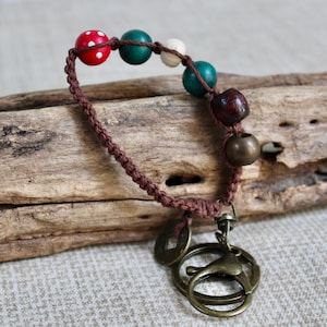 May include: A handmade keychain featuring a brown macrame cord with colorful wooden beads in red, green, and white. The keychain includes bronze-colored metal rings and decorative coin charms.