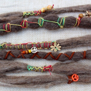 May include: Brown synthetic dreadlocks with colorful string and leather accents. The dreadlocks are decorated with peace sign charms, a wooden flower charm, and wooden beads.
