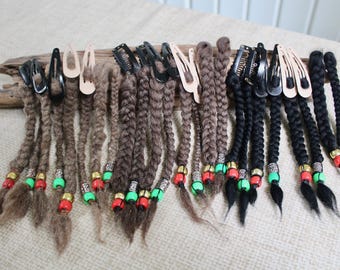 May include: A collection of hair clips featuring attached braided hair extensions in shades of brown and black. Each braid is secured with colorful beads in red, green, and metallic silver tones, attached to metal snap clips in black or beige.
