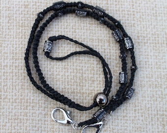 Soporte para gafas negro con macramé de cáñamo negro y cuentas de plata grabadas.