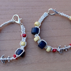 May include: Two white cord bracelets with blue and red wooden beads and silver anchor charms.