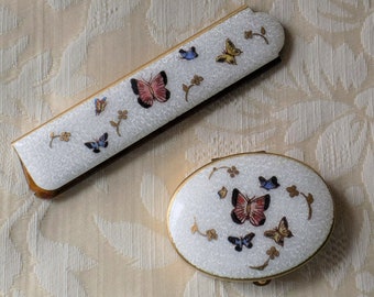 Könnte beinhalten: Ein Set aus zwei weißen Kompaktbehältern mit goldenen Verzierungen und Schmetterlingsmotiven. Der größere Behälter ist rechteckig und der kleinere oval.