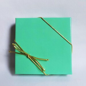 K&ouml;nnte beinhalten: Eine mintgr&uuml;ne Geschenkbox, die mit einem goldenen Band gebunden ist.