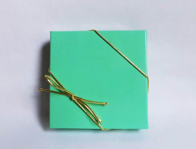 K&ouml;nnte beinhalten: Eine mintgr&uuml;ne Geschenkbox, die mit einem goldenen Band gebunden ist.