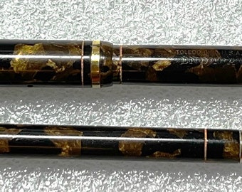 May include: A black and gold fountain pen and matching pencil set with a marbled design. The pen has a gold clip and the pencil has a gold band.