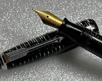 May include: A black fountain pen with a gold nib is displayed. The pen's body has a black and silver striped pattern. The pen's nib is gold-colored, and the pen cap is open, revealing the pen's inner workings. The pen is a classic writing instrument.
