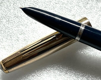 May include: A gold and blue fountain pen with a gold cap and a blue barrel. The pen has a fine nib and a clip on the cap.