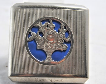 May include: Silver compact with a blue enamel floral design and the words "Cara Nome" engraved on the bottom.