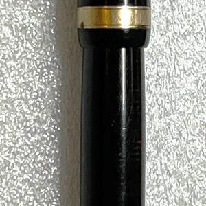 May include: A black fountain pen with gold-colored accents. The pen has a sleek, cylindrical design with a gold band near the center and a gold-colored clip. The pen is a classic writing instrument.