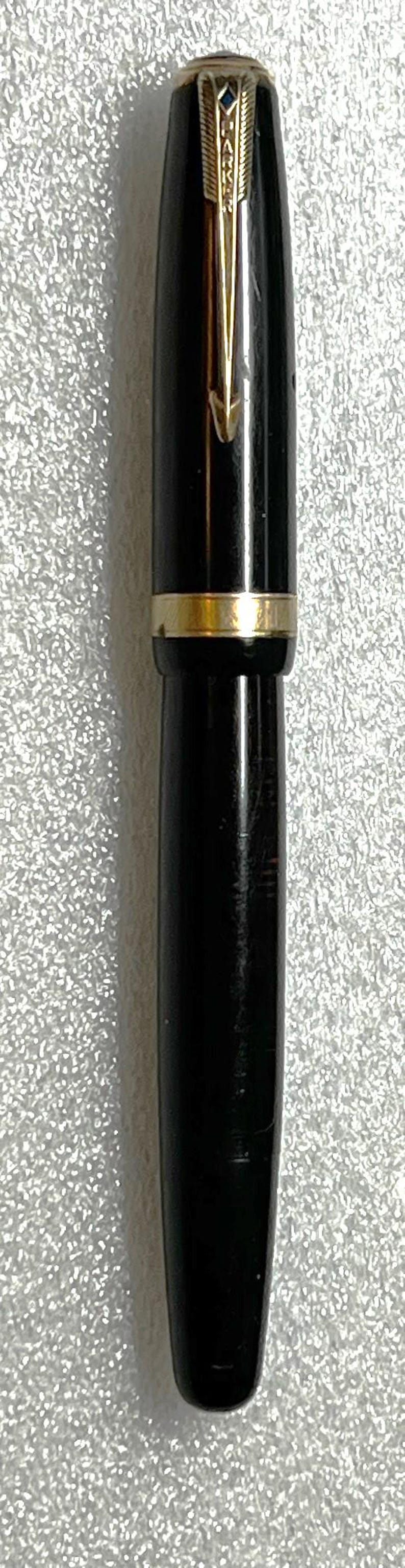 May include: A black fountain pen with gold-colored accents. The pen has a sleek, cylindrical design with a gold band near the center and a gold-colored clip. The pen is a classic writing instrument.