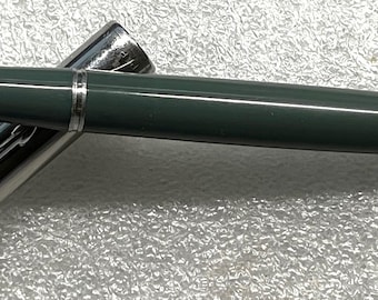 May include: A vintage fountain pen with a dark green barrel and a silver-colored cap. The pen is lying on a textured surface, with the cap partially open, revealing the nib. The pen has a classic, streamlined design.
