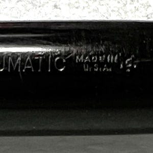 May include: Close-up of a black pen with the word "VACUMATIC" engraved on the side. The text "MADE IN U.S.A." is also visible. The pen has a shiny, reflective surface.