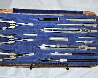May include: A vintage compass set in a brown leather case with a blue velvet lining. The set includes a variety of compasses, rulers, and other drafting tools.