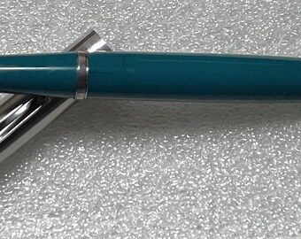 May include: A teal blue fountain pen with a silver cap and a silver body. The pen is lying on a white surface.