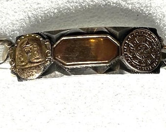 May include: Silver-tone curb chain bracelet with a rectangular clasp. The center features three decorative elements: a gold-tone medallion, a gold-tone plaque, and a circular medallion. The bracelet is a jewelry item.