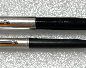 May include: Two black and silver pens, one with a clip and the other with a cap. Both pens have a silver band with a gold stripe.