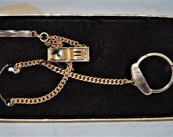 May include: A gold-tone key chain with a small, rectangular charm that says "JB" in black lettering. The chain is attached to a gold-tone key ring.