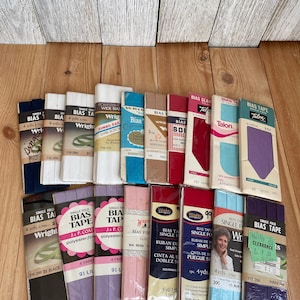 May include: Assortment of bias tape in various colors and patterns, including black, white, purple, pink, blue, and red. The tape is packaged in small, rectangular boxes with labels that include the brand name "Wright's" and "Talon".