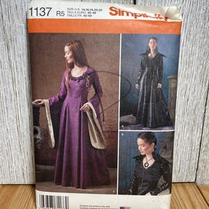 May include: Simplicity sewing pattern featuring medieval-style gowns. The pattern packet shows a woman in a long purple dress with long sleeves and a woman in a black gown. The pattern includes sizes 14-22.