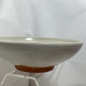 May include: A handmade ceramic bowl with a light gray glaze. The bowl has a wide, shallow shape and a slightly textured surface. The base is a warm brown color. This bowl is perfect for serving salads, soups, or other dishes.