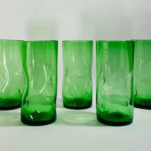 May include: A set of five cylindrical drinking glasses in a vibrant emerald green color. Each glass features a distinct, irregular rippled texture along the sides, creating a wavy, organic appearance with a smooth, flat base and rim.
